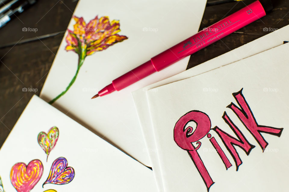 Pink Faber-Castell fine artist pen with word pink colored in on paper sketch pads and drawings of flowers and hearts 