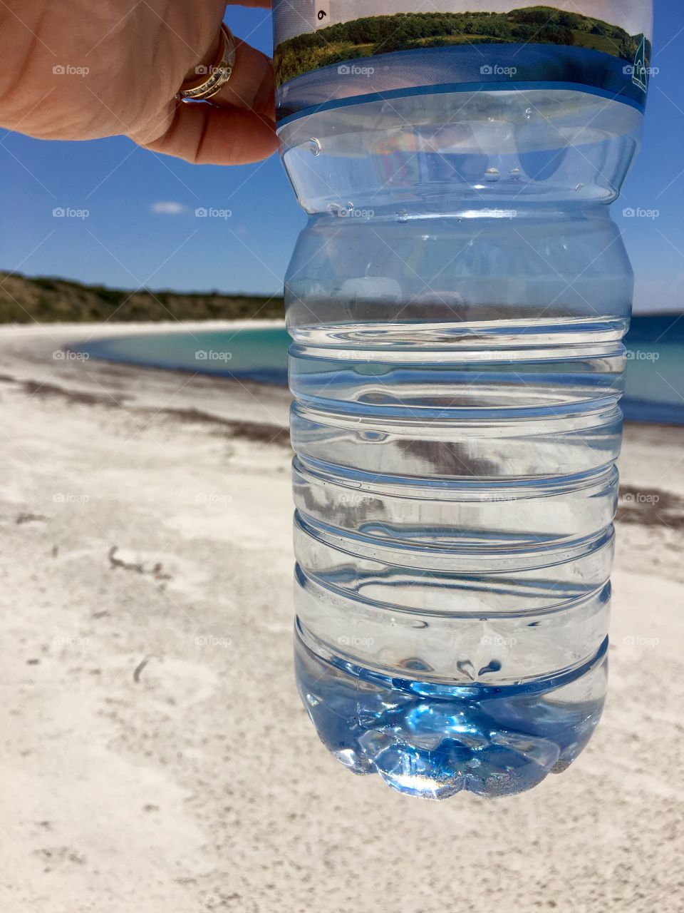 Woman’s hand holding refreshing bottle of spring water closeup with ocean horizon visible through the bottle 