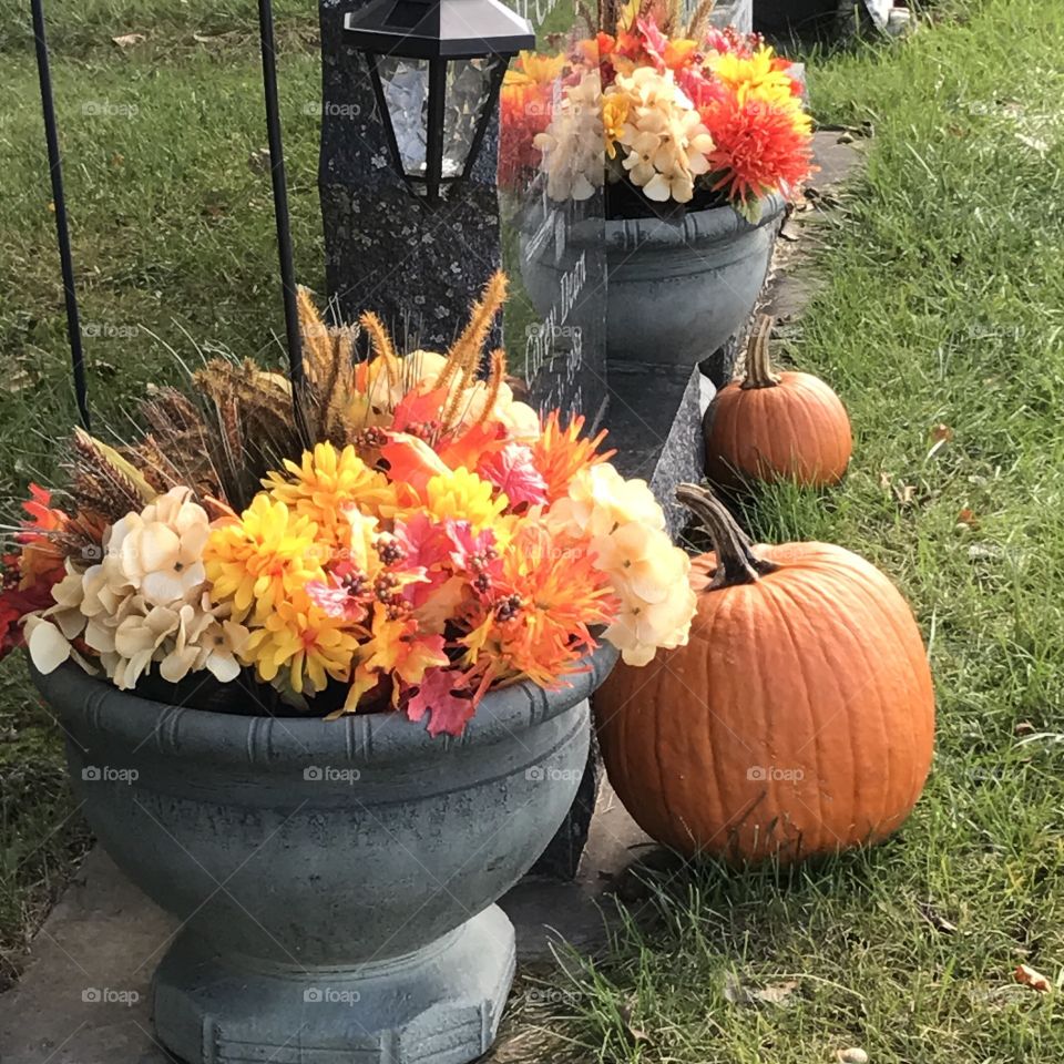 A headstone at a cemetery decorated for autumn.