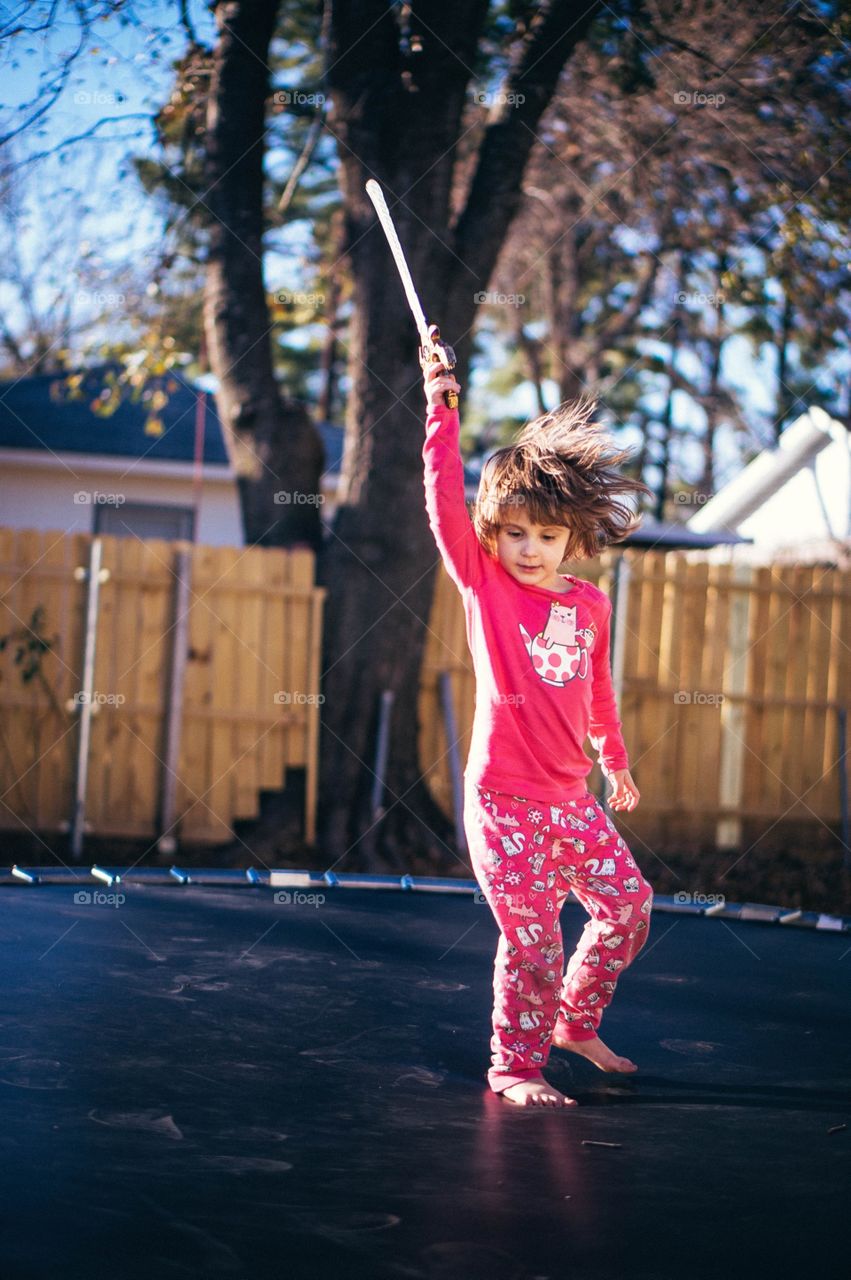 Girl standing on trampolining and holding sword