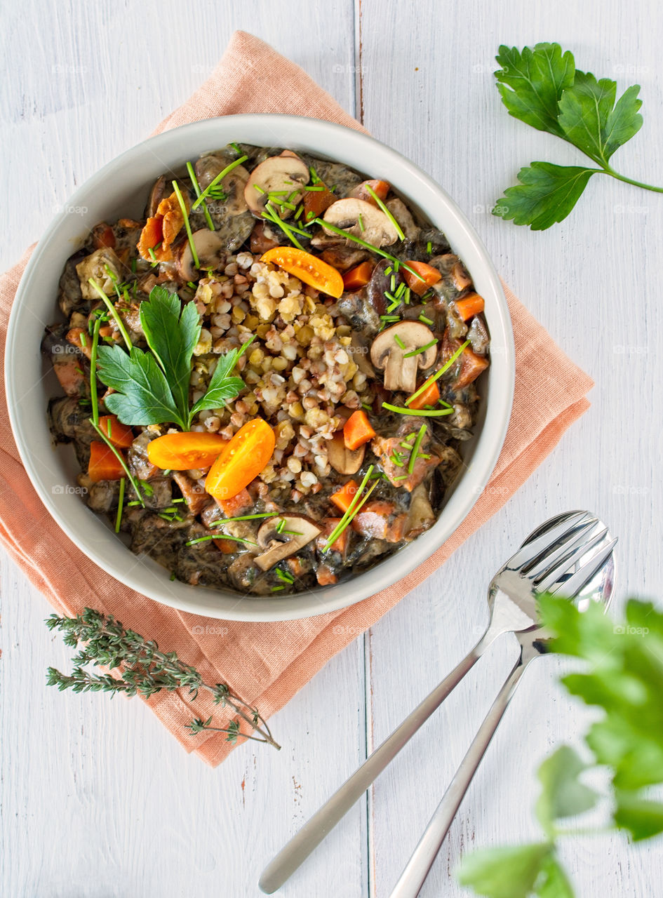 Vegan buckwheat Buddha bowl with Champignons, yellow tomatoes and greens on a white wooden table, view from above. Vegan healthy meal, nutritional lunch