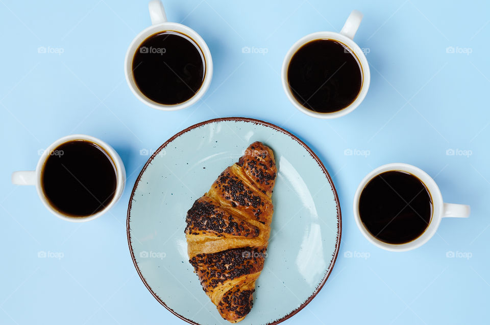 Business working morning with cup of hot coffee, fresh delicious croissant on blue background close up. Top view, copy space, flat lay, mockup.