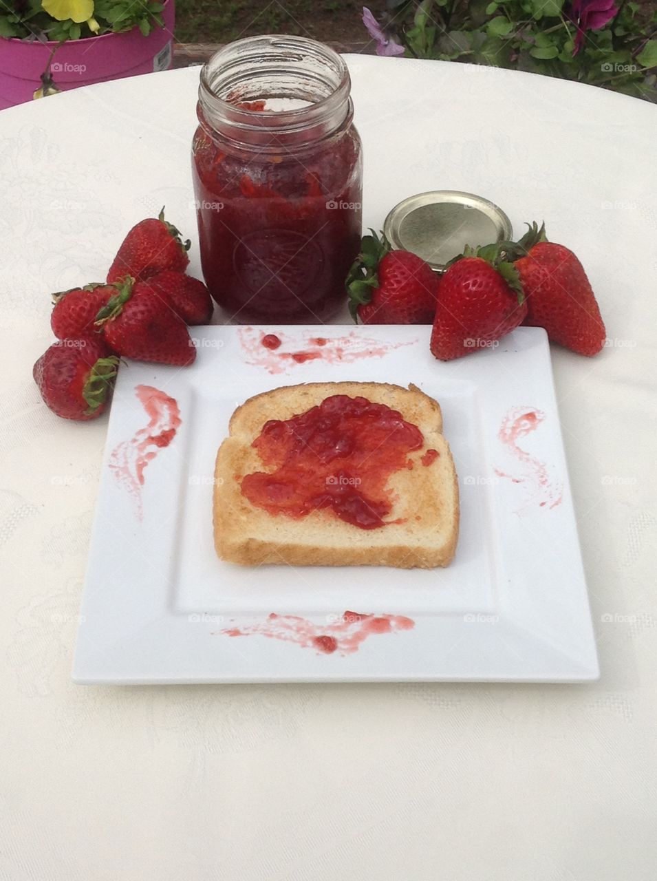 Homemade strawberry jam in a jar with a slice of toast.