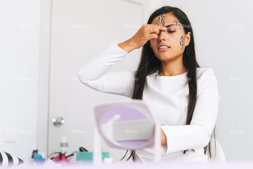 Long hair brunette woman with facial massage tape against mirror in office room spa salon 