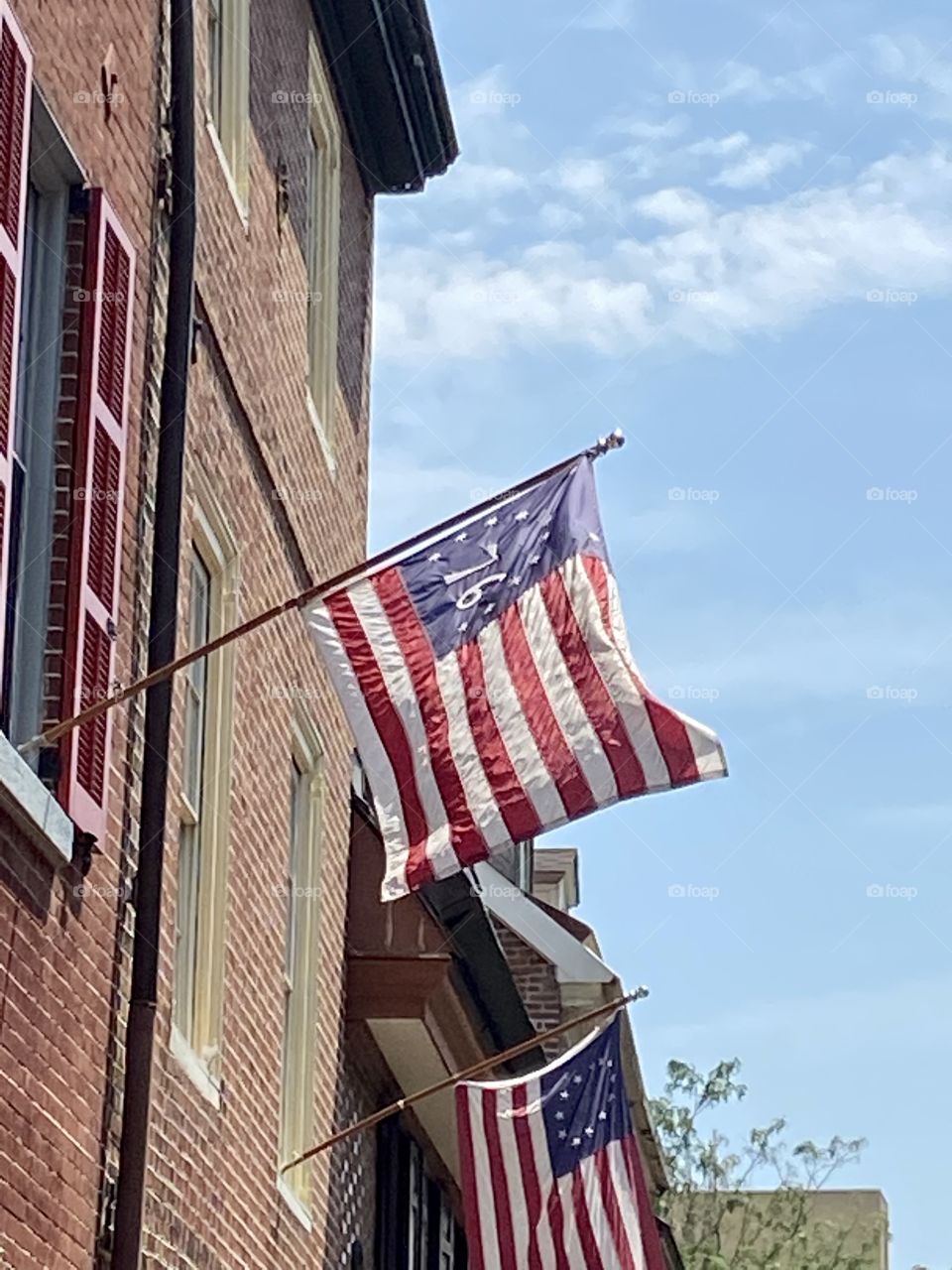 An old-fashioned American flag with thirteen stars and the number 76 flying from a poke attached to a brick row house