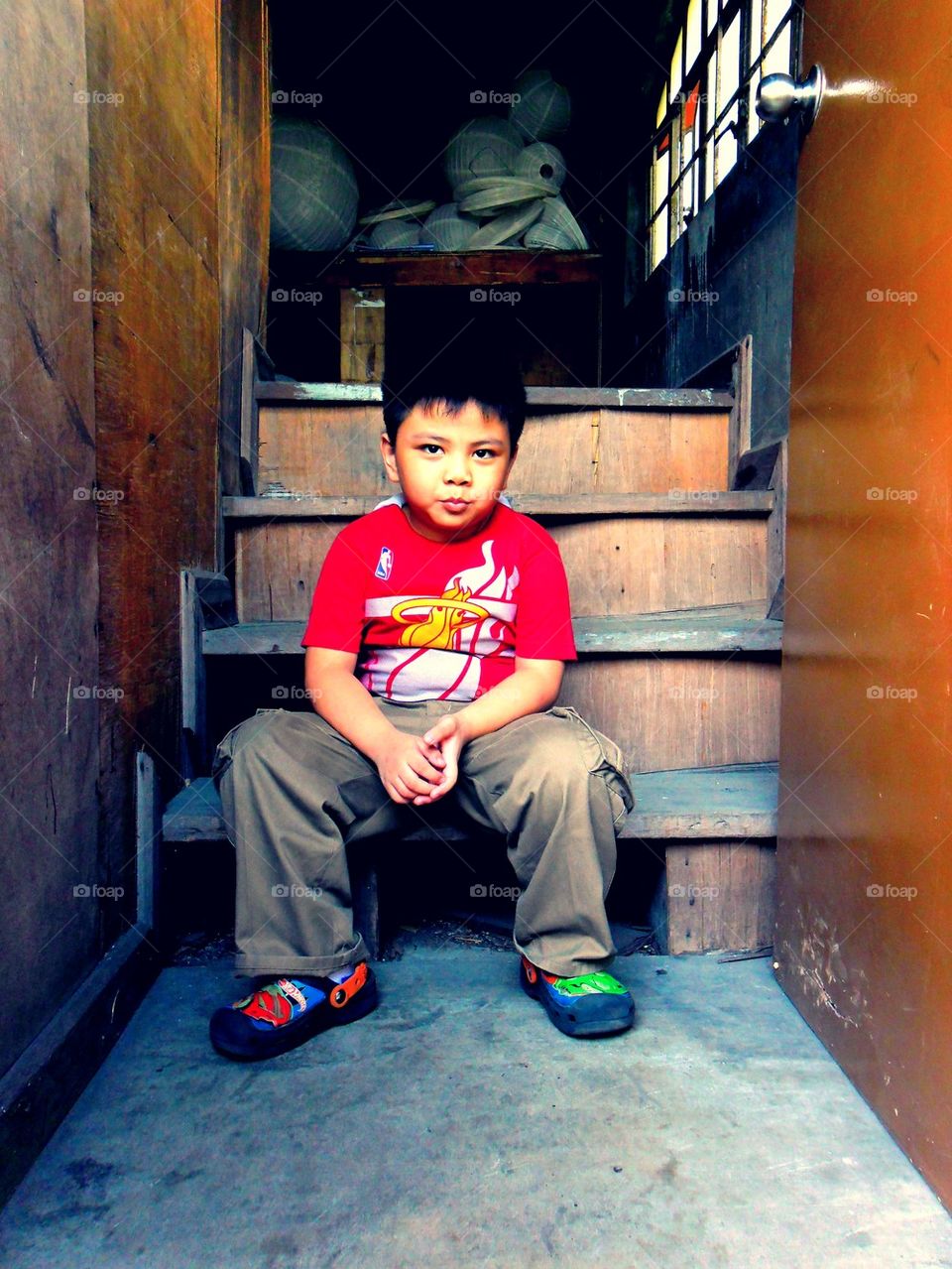 Young asian kid sitting by the steps of a staircase by a doorstep