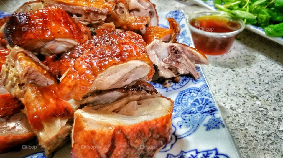 Cantonese roast duck, presented on a plate in pieces, accompanied by a small tub of plum sauce. The duck has a shinning red-brownish skin frequently seen hanging behind shop windows.