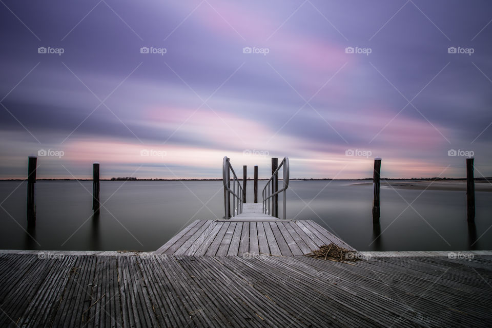 Symmetrical dock with ramp leading to smooth calm water. Painterly soft pastel colored clouds streaking across the sky. 