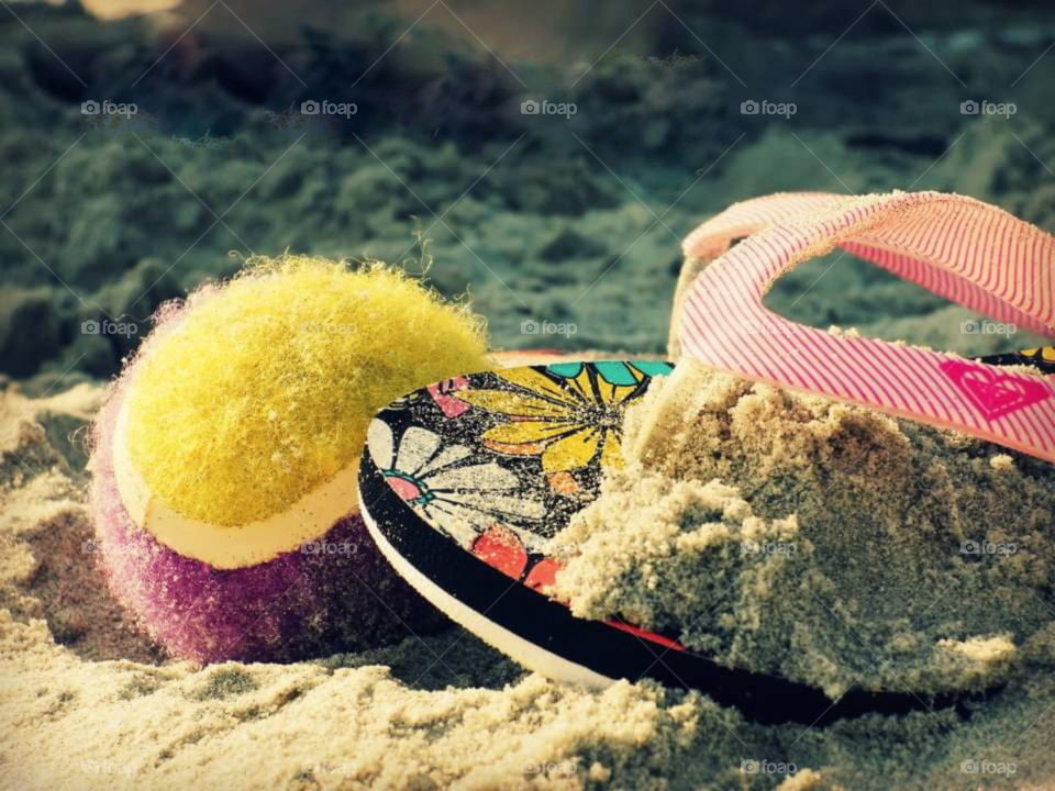 Flip flop and tennis ball left on Sandy beach by a child in a hurry to play.