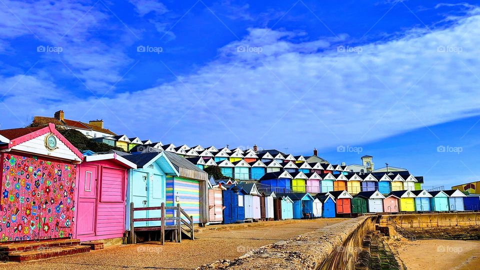 Sunlit tiers of bright coloured beach huts with a bright blue sky and cloud formations