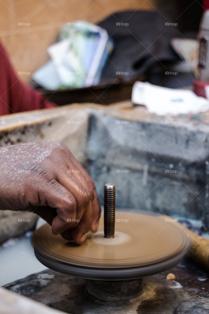 This man's job is to use this machine to turn big stones into lovely little soft and clear pieces of gems, to be used later as accessories or part of decoration. You will see different angles of the same hand and job.