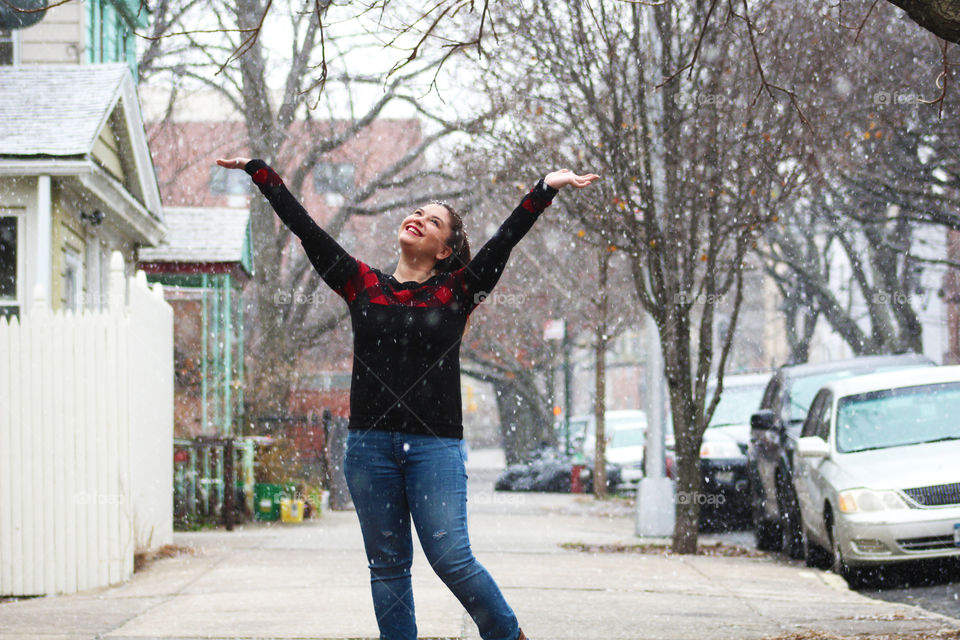 Woman standing in the snow wearing a Christmas sweater and jeans. 