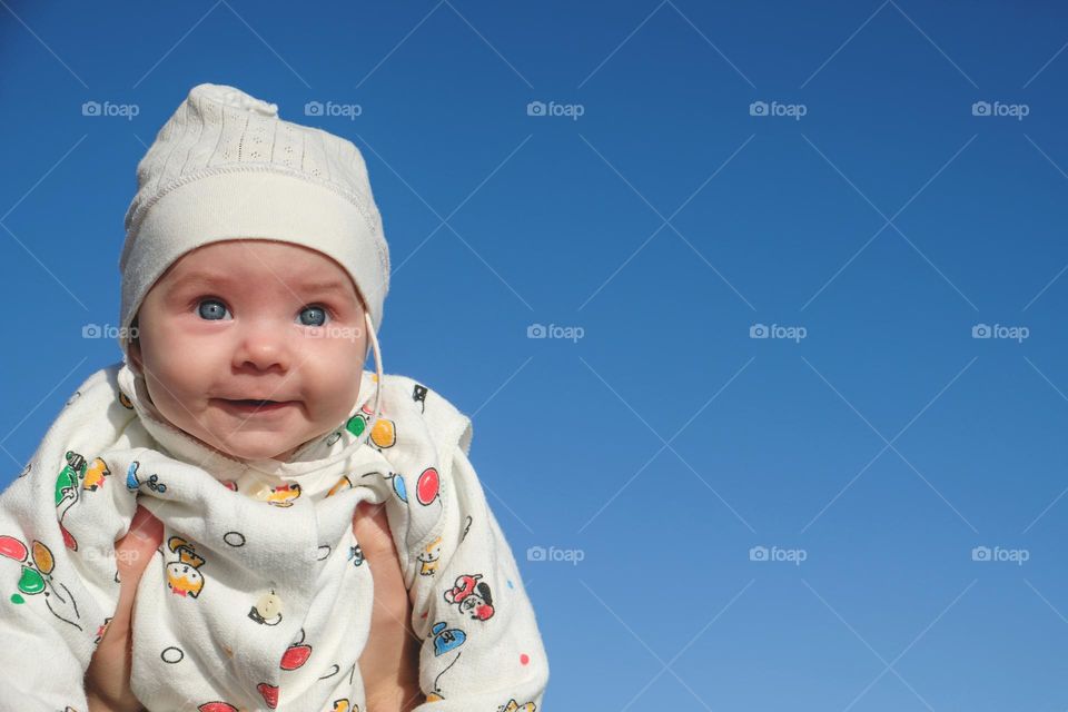 Smiling baby in white hat with blue sky on the background