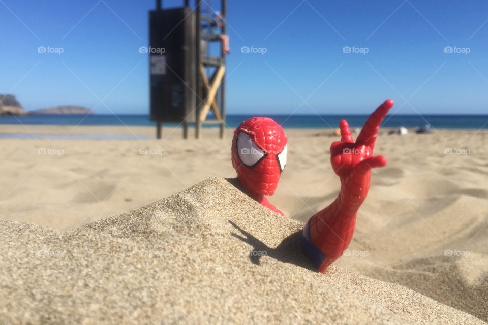 Spider-Man is buried in the sand on a beach