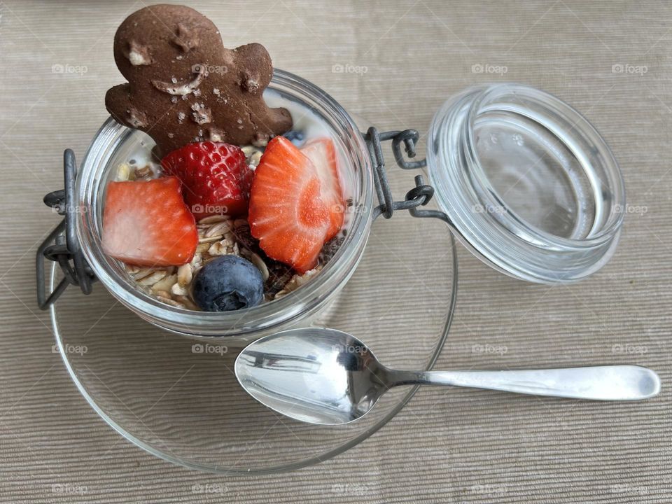 Breakfast with yoghurt in a glass and oat flakes as well as berries and a cookie.