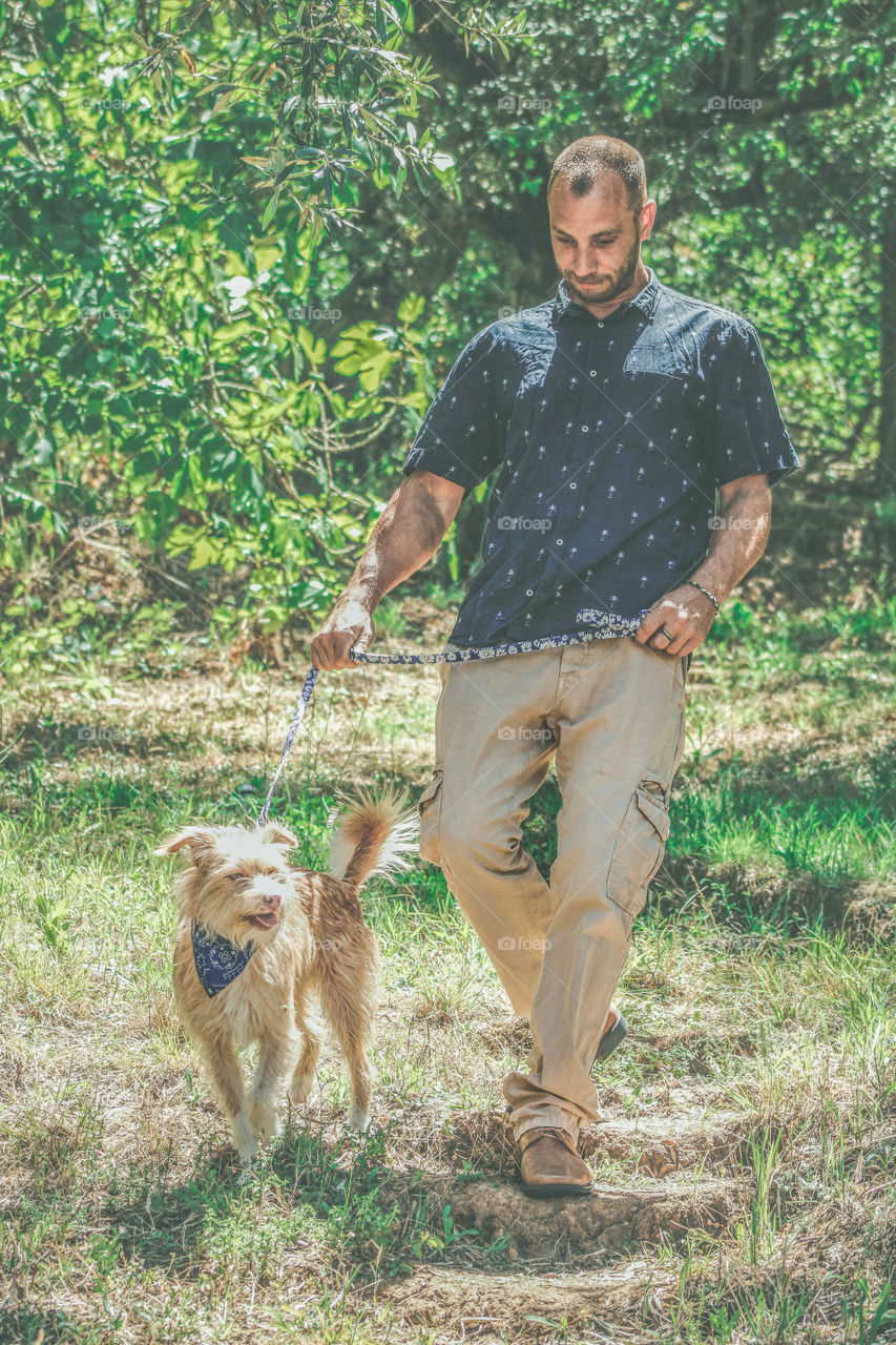 A man takes his dog for a walk through a green park on a bright, sunny morning. The colour of the dogs coat and collar, tone in with the man’s outfit