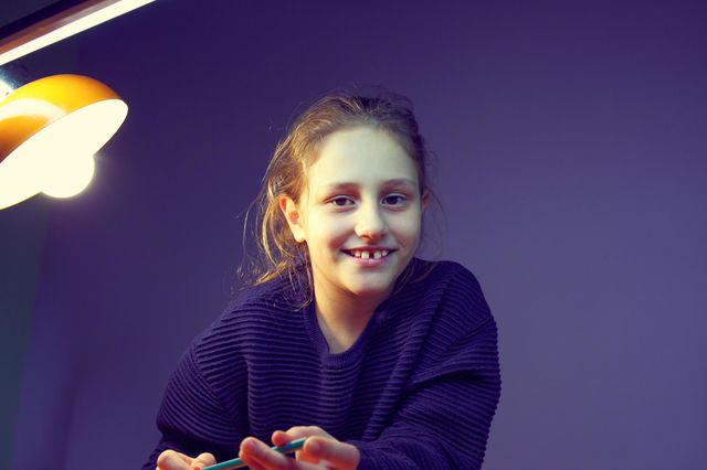 the girl is doing her homework and is distracted smiling at the camera. purple background