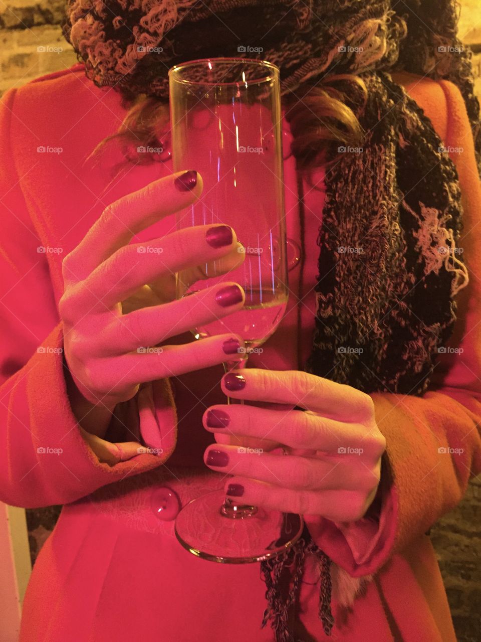 Woman hands wearing red nail polish holding glass of champagne outside 