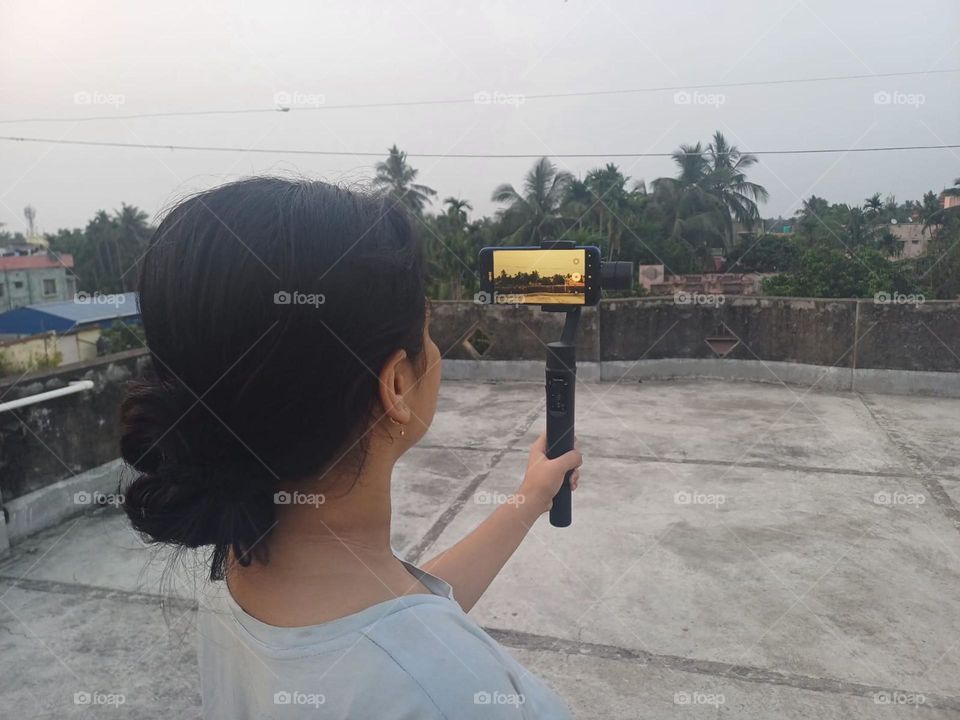 One girl is engaged to create a video on the rooftop with her Smartphone and gimbal.