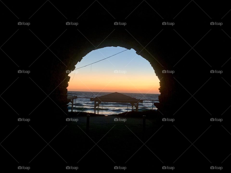 Sunset over the sea with beach huts view through old stones arch