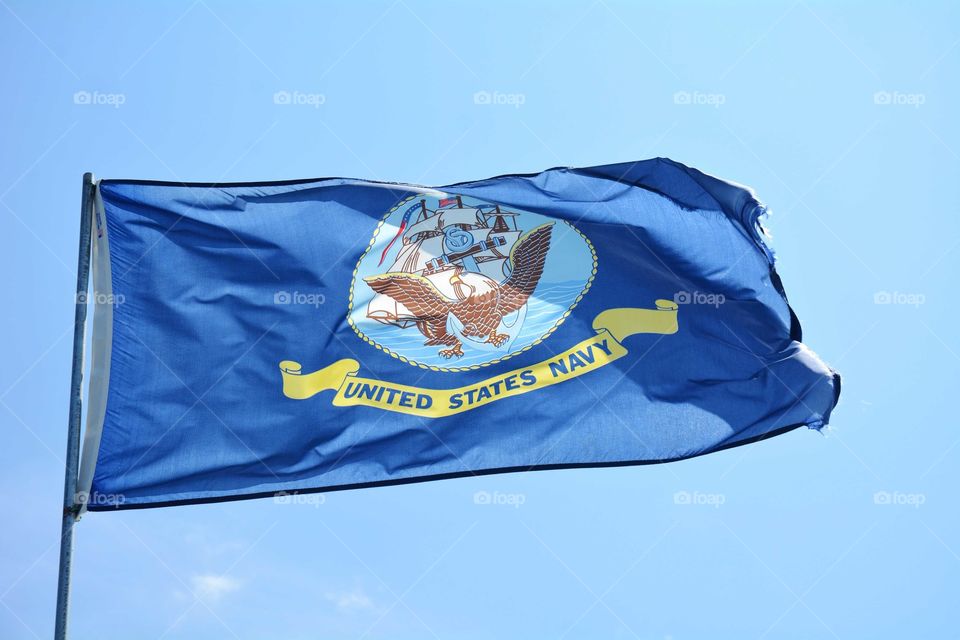 United States Navy flag blows against a blue sky.
