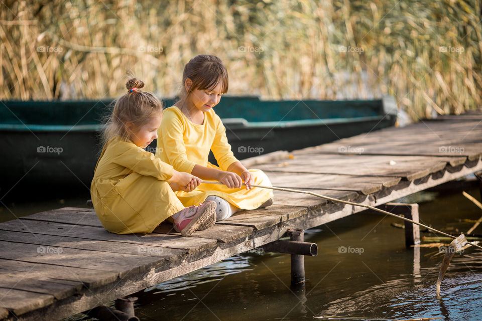 Little sisters playing near lake at autumn day 