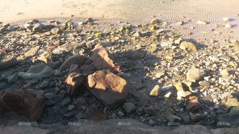 A bunch of stones washed up on a bay, so clear that you can see the ripples in the sand
