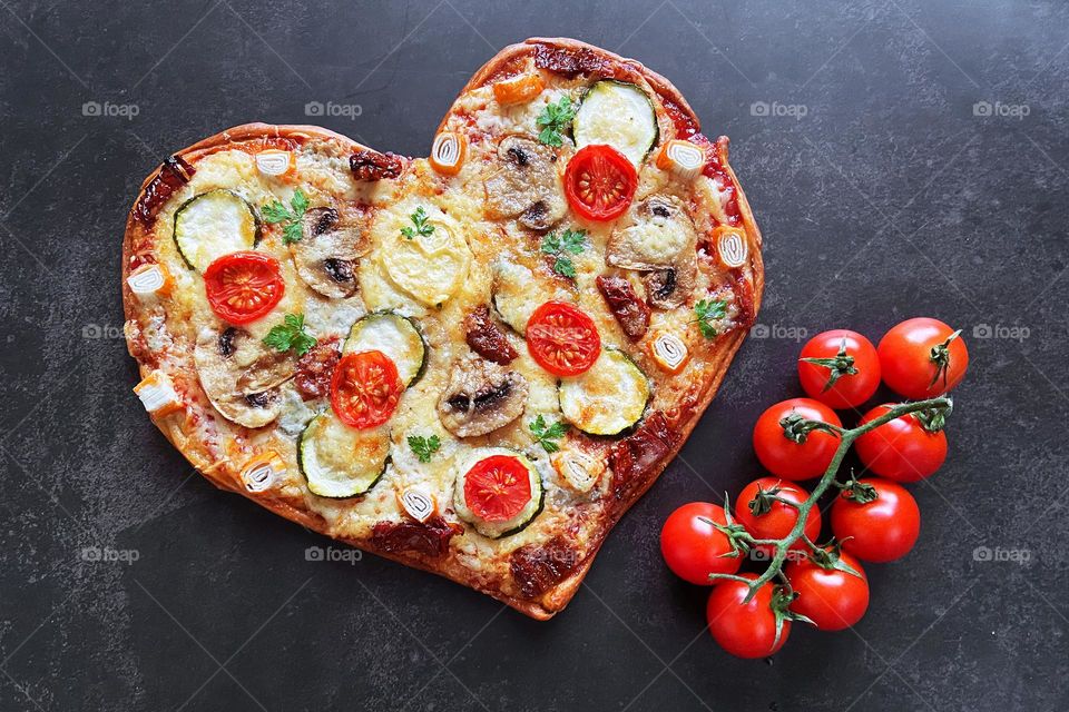 Top view of delicious heart shaped pizza with mozzarella, zucchini and tomatoes for Valentines day close up. Black background