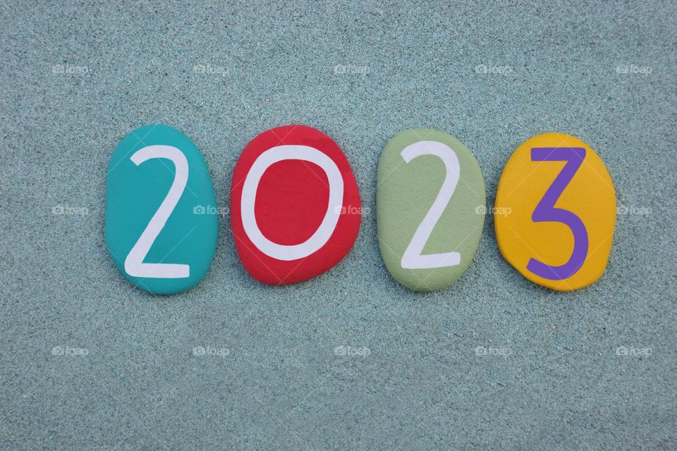 Year 2023 composed with multi colored stone letters over green sand