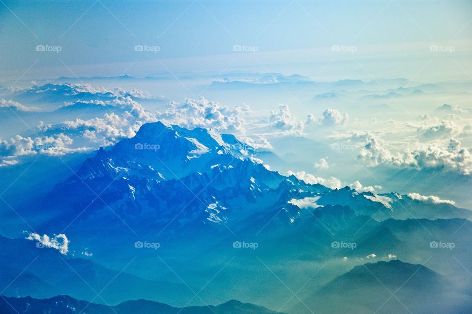 A bird's eye view on a snow-capped mountain range with clouds obscuring the horizon
