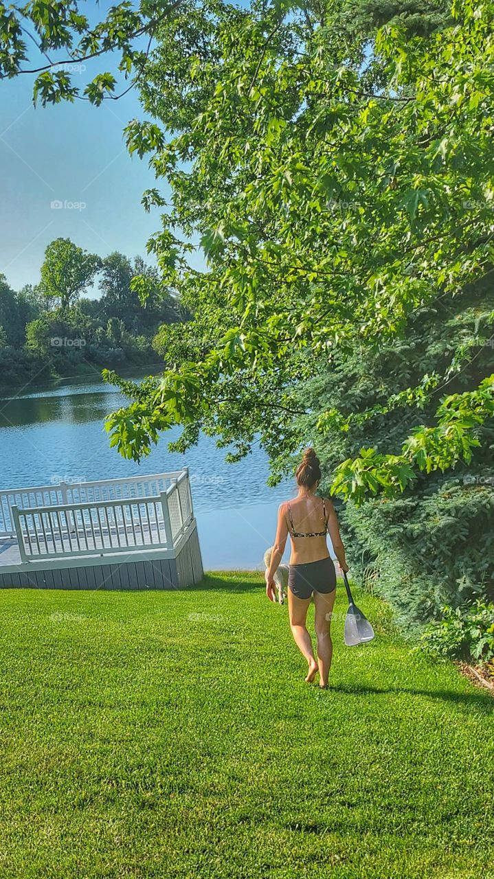 woman walks towards Lake with paddle
