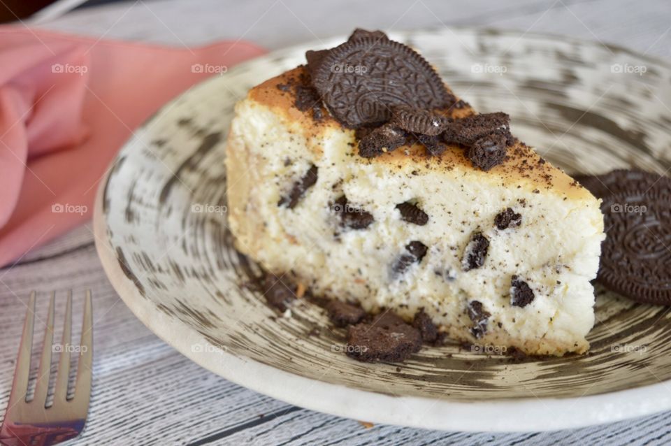 Oreo cookie cheesecake on a high contrasting play with a pink napkin on a white rustic background