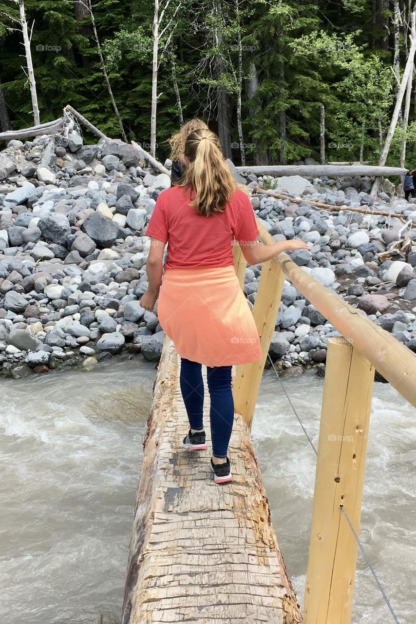 A group of young hikers cross a tree bridge over the glacial waters of Mount Rainier National Park 