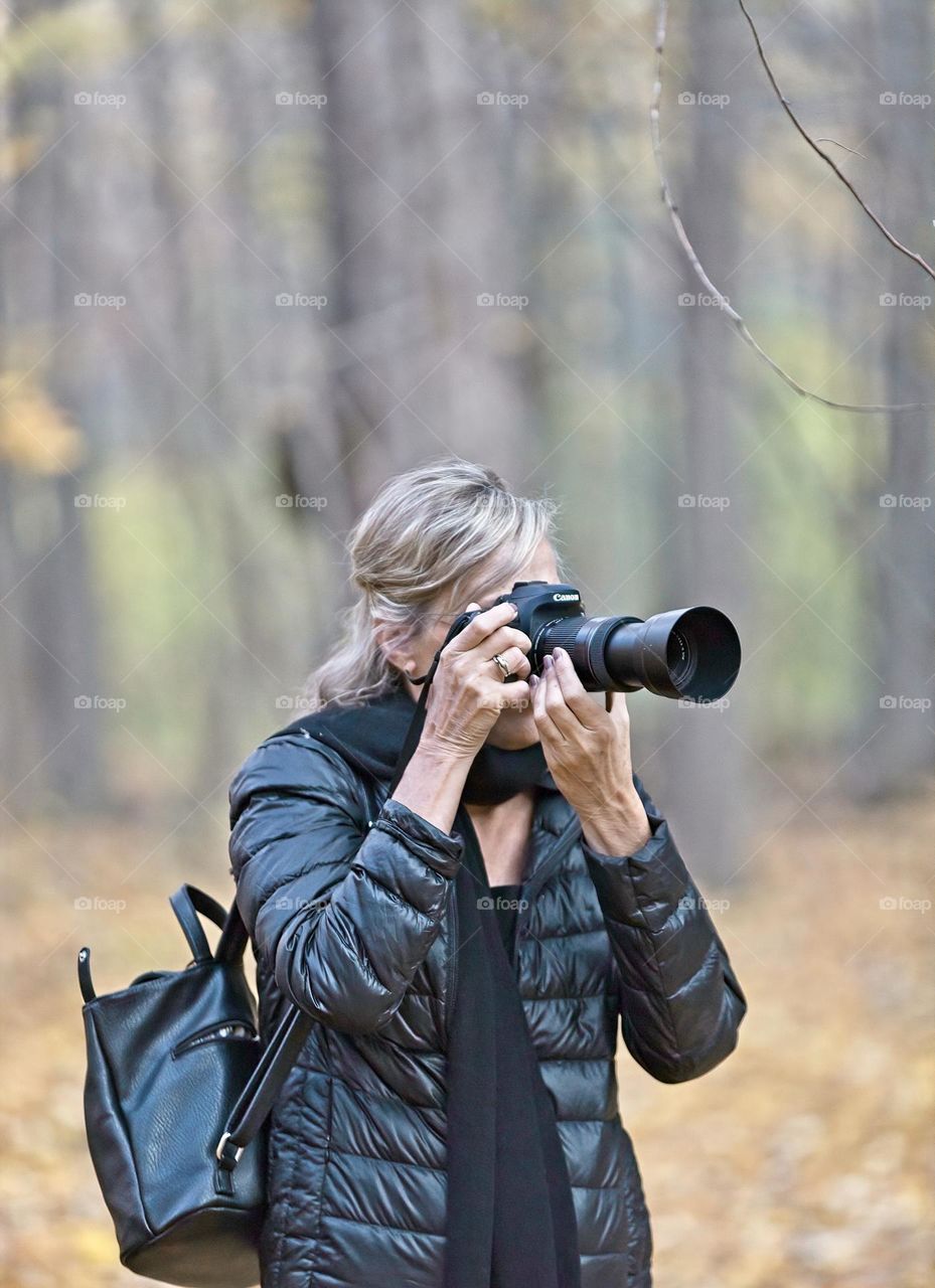 On a self assignment shooting for FOAP—South Australia, female photographer with camera outdoors, blurred forest background, autumn