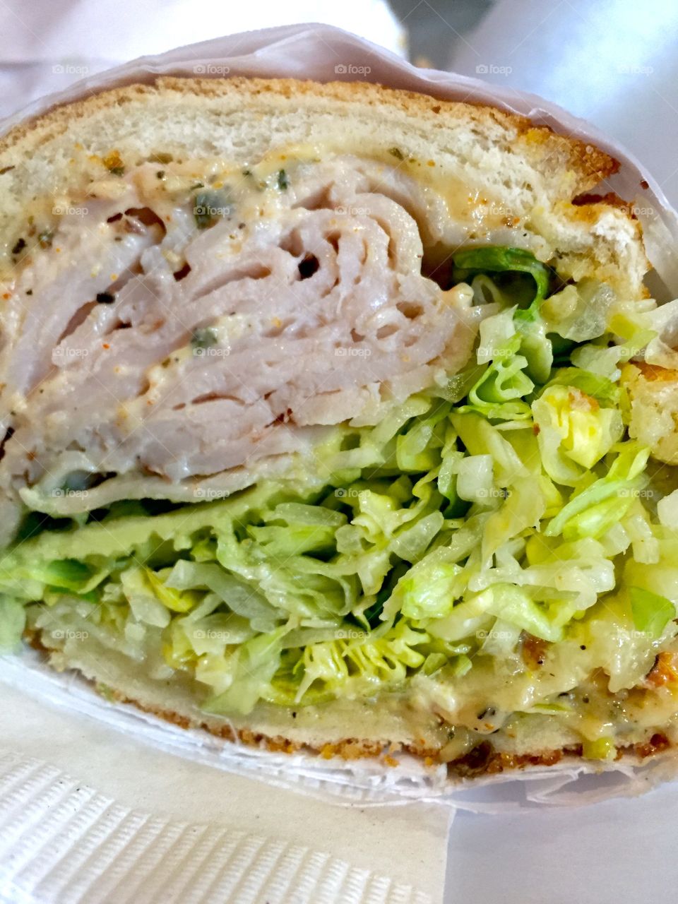 Packed submarine sandwich cut in half featuring turkey, melted cheese, shredded lettuce, and condiments.