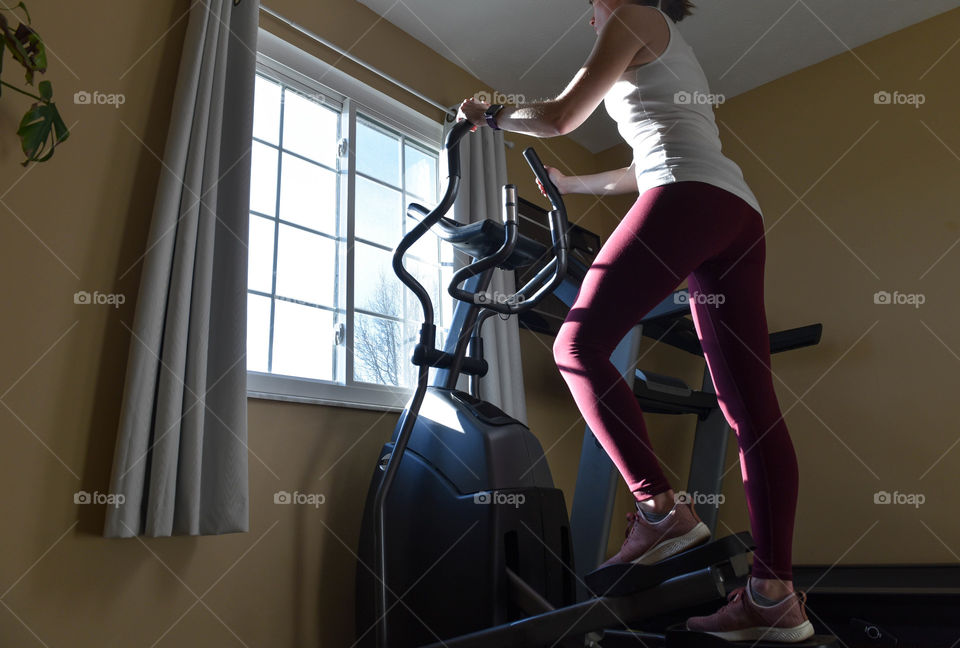 Young woman exercising on an elliptical machine in front of a window at sunrise