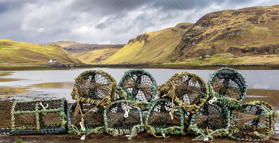 Lobster pots line the beach of a loch, with hills and dark clouds in the background, Isle of Skye 