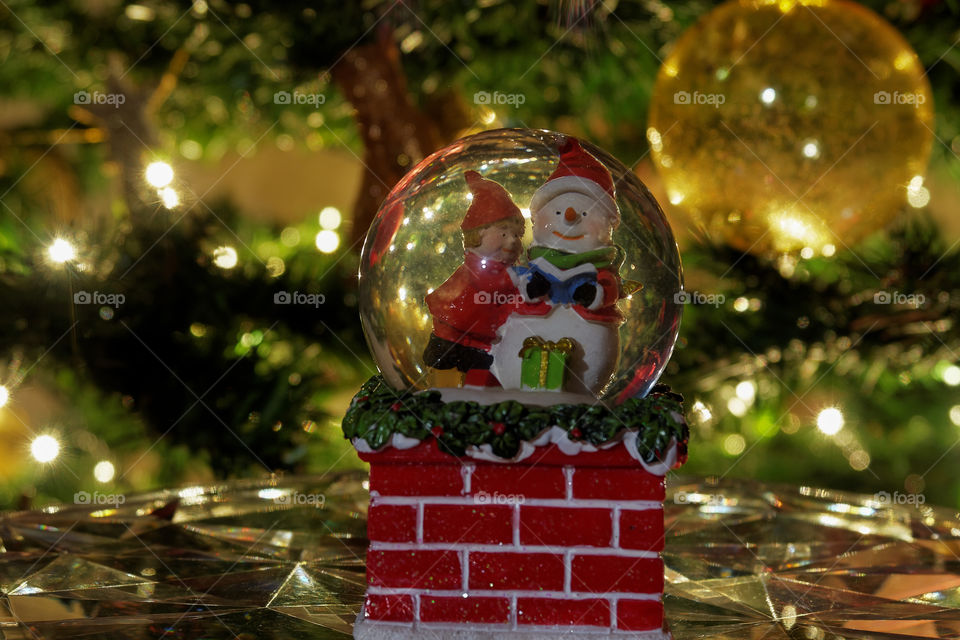 Christmas snow globe ball. Decorating Christmas dome ball before a lit Christmas tree.