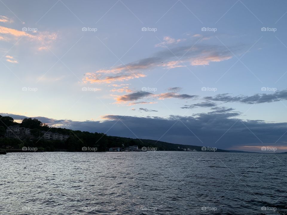 There is a beautiful sunset over a calm lake with a hill in the background. It is a calming scene with cool colors and calming to the eye.