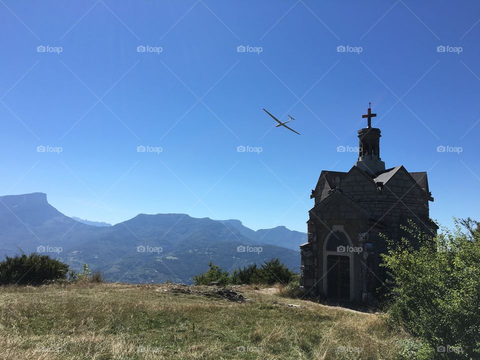 Glider around mountain chapel in summer sky 