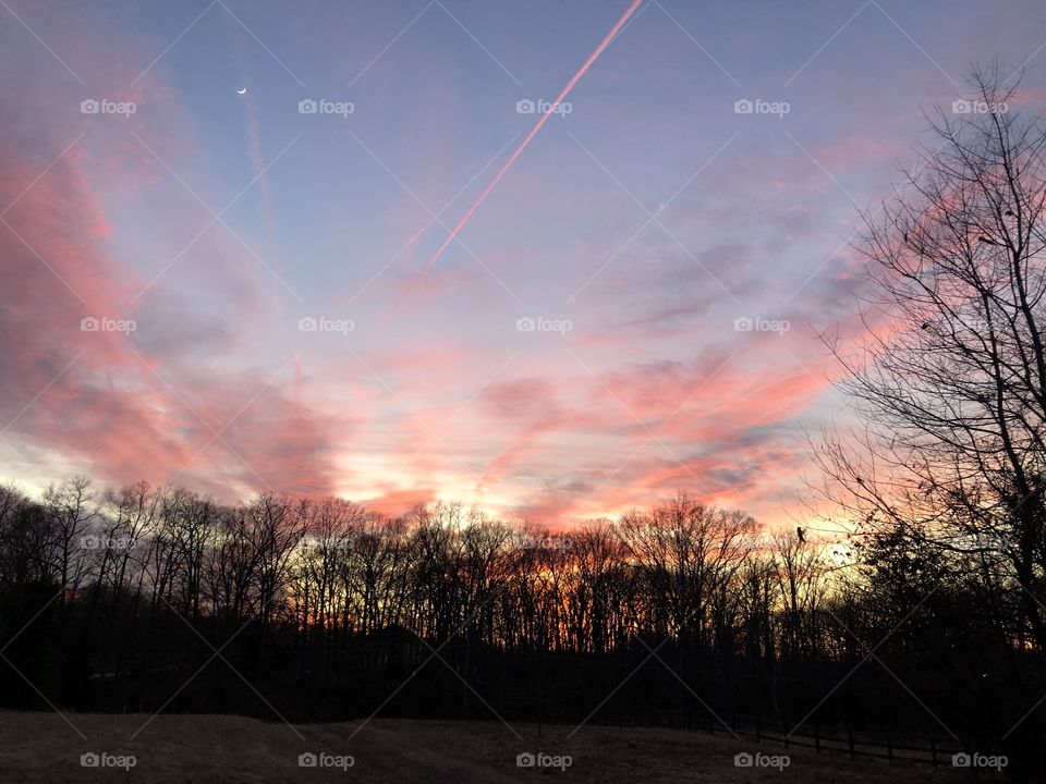 An incredible Virginia sunset shows orange, pink, and blue in the sky complete with an amazing contrail and a crescent moon