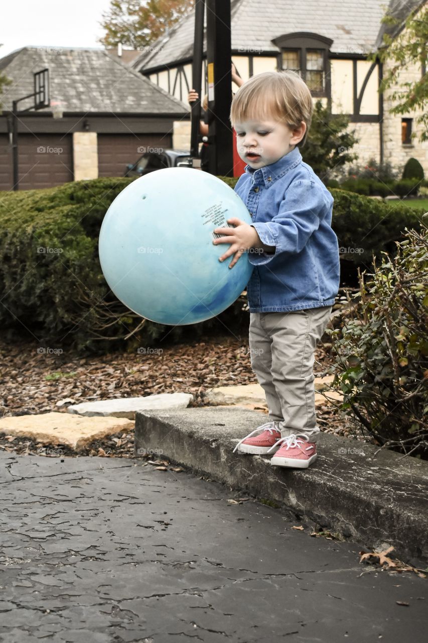 Cute 19 month toddler boy in blue denim shirt playing outdoors 