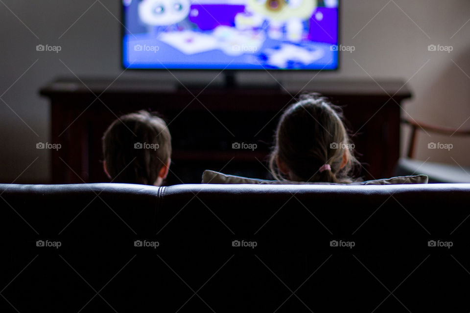 Loved this moment of these two little kids watching TV and the light shining on them. Image of two kids sitting and watching television.