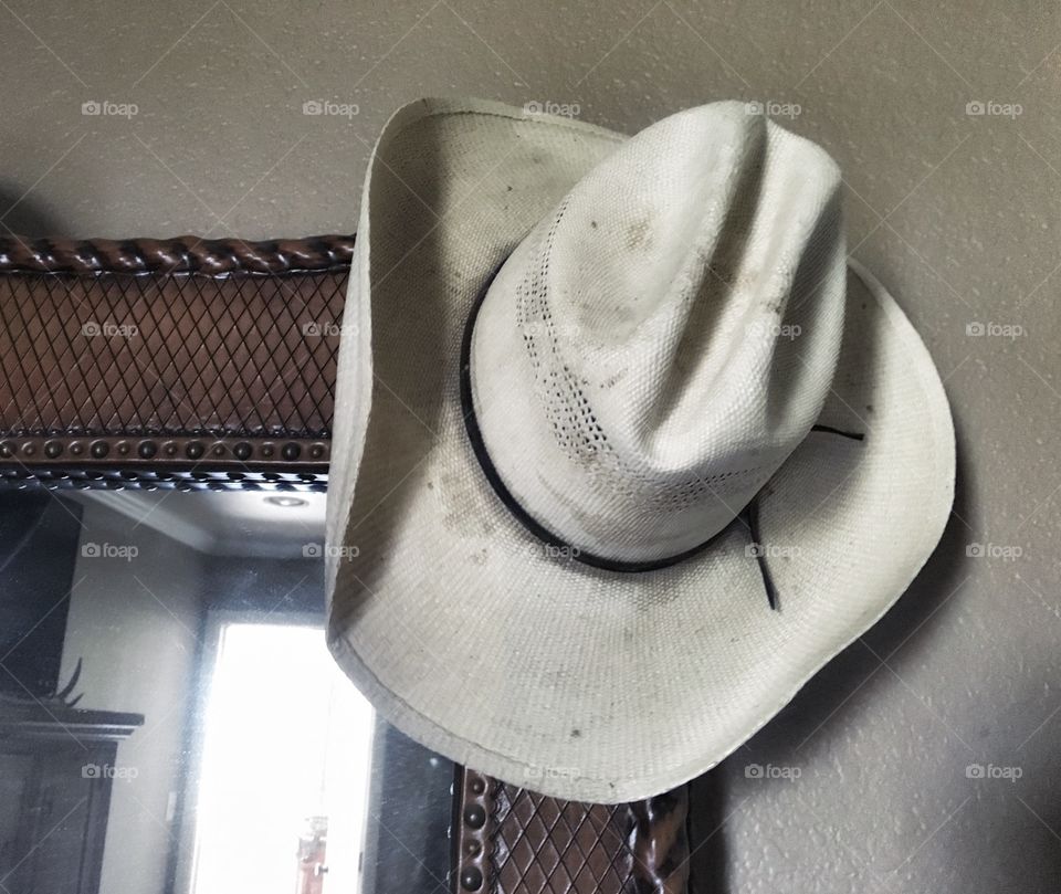 Straw cowboy hat hanging on a tooled leather mirror. 