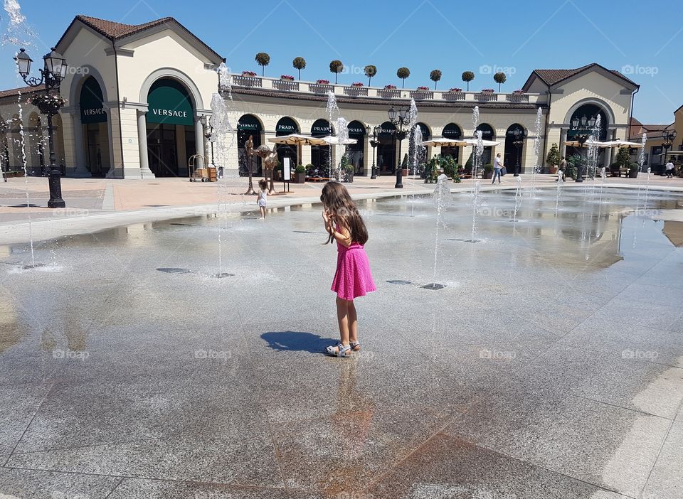 Little girl playing with the water in a big fountain