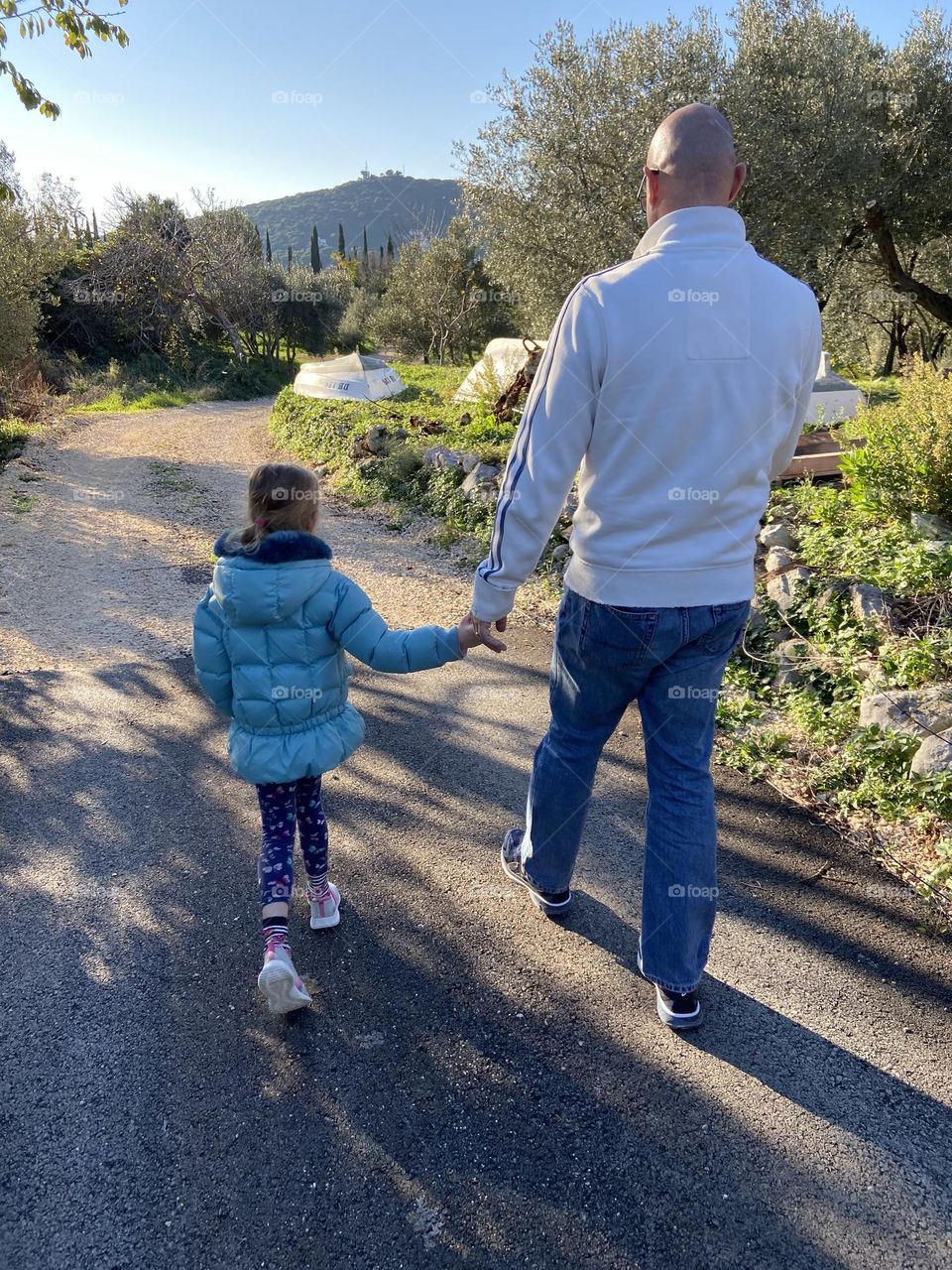 Father holding daughter’s hand during a walk.