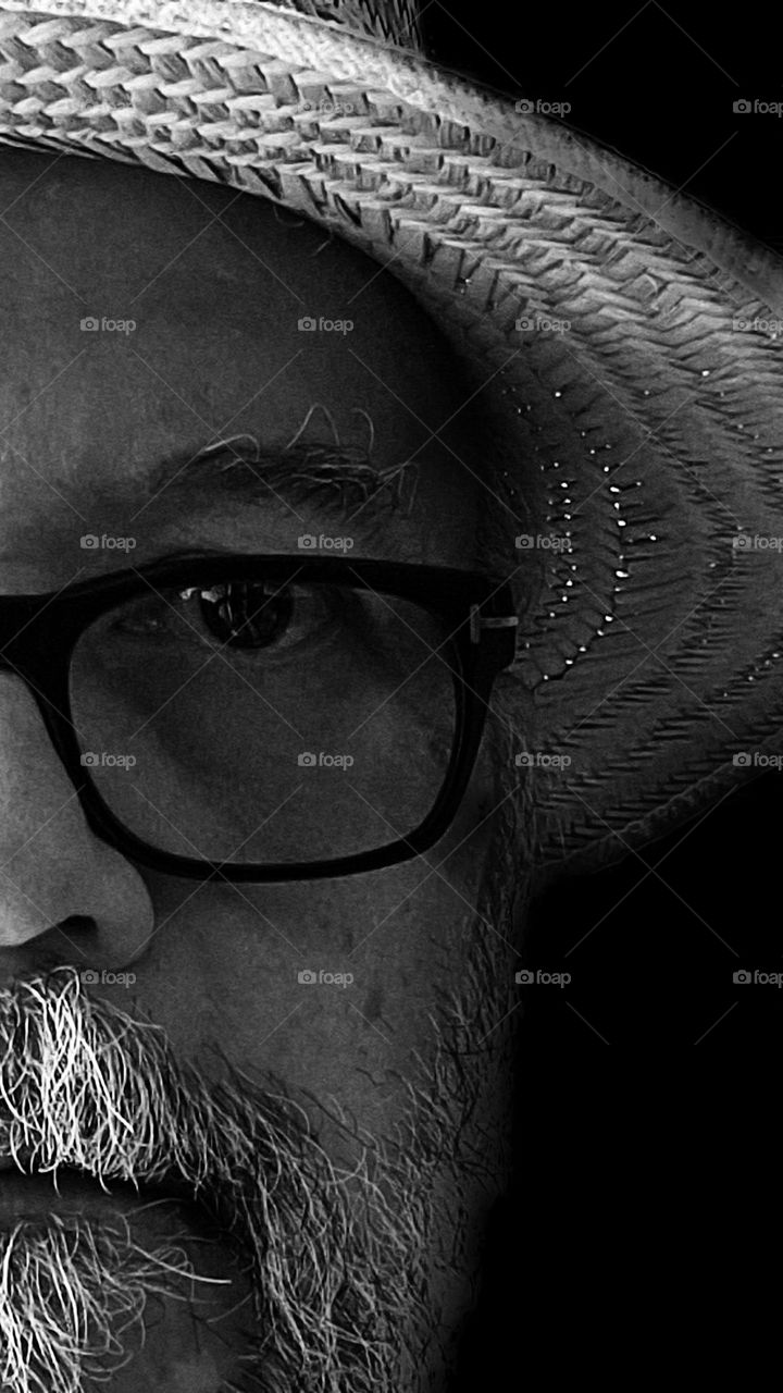 Half of the face of a man with a beard, wearing glasses and a straw hat. Natural light falls on the face and hat.
Metade da face de um homem com barba, usando óculos e chapéu de palha.Luz natural incide sobre a face e chapéu.