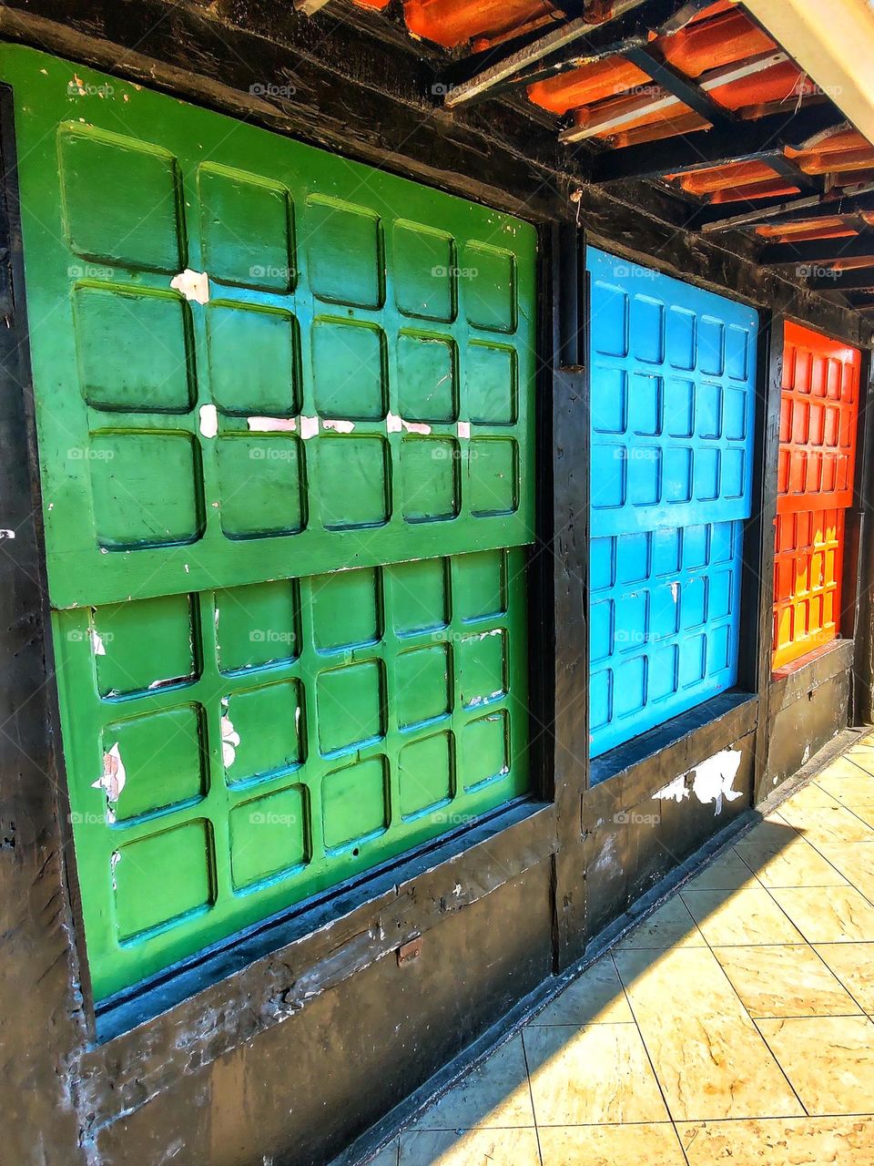 three square wooden windows, forming several small squares, painted green, blue and red.