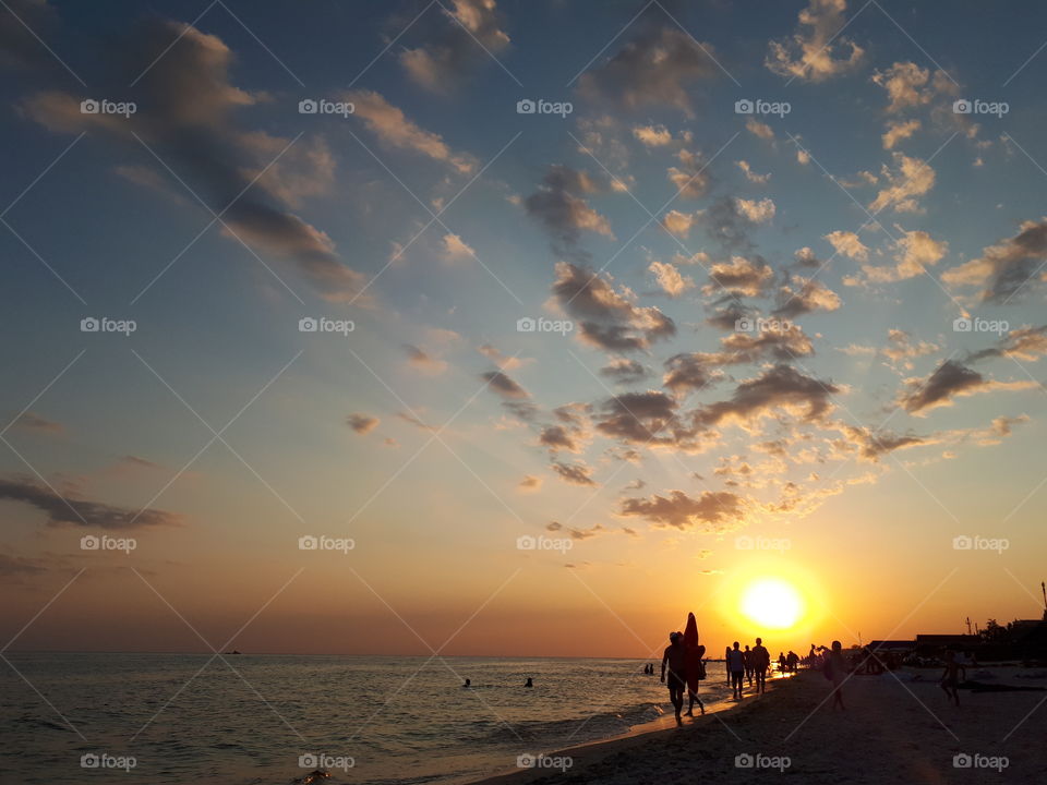 People walk along the beach at sunset time