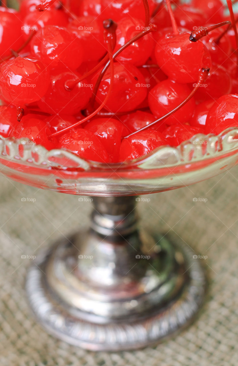 Red maraschino cherries perched in a vintage clear glass pedestal dish